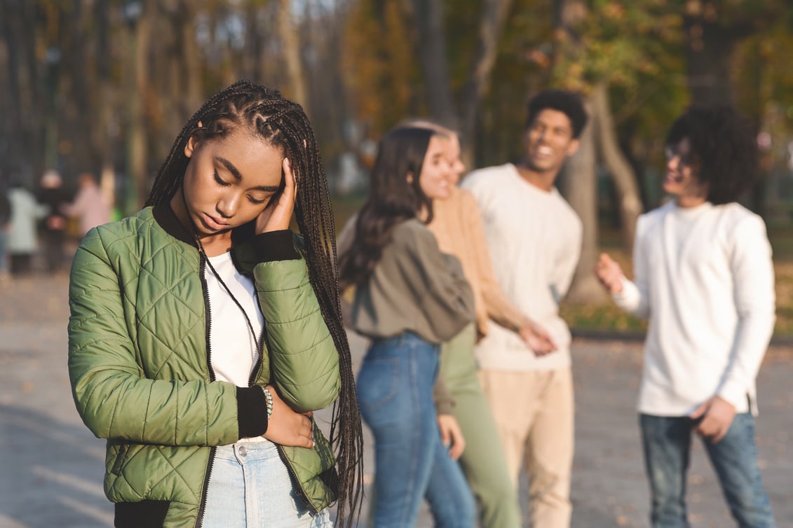 Upset Teen Black Girl With Friends Gossiping In Background