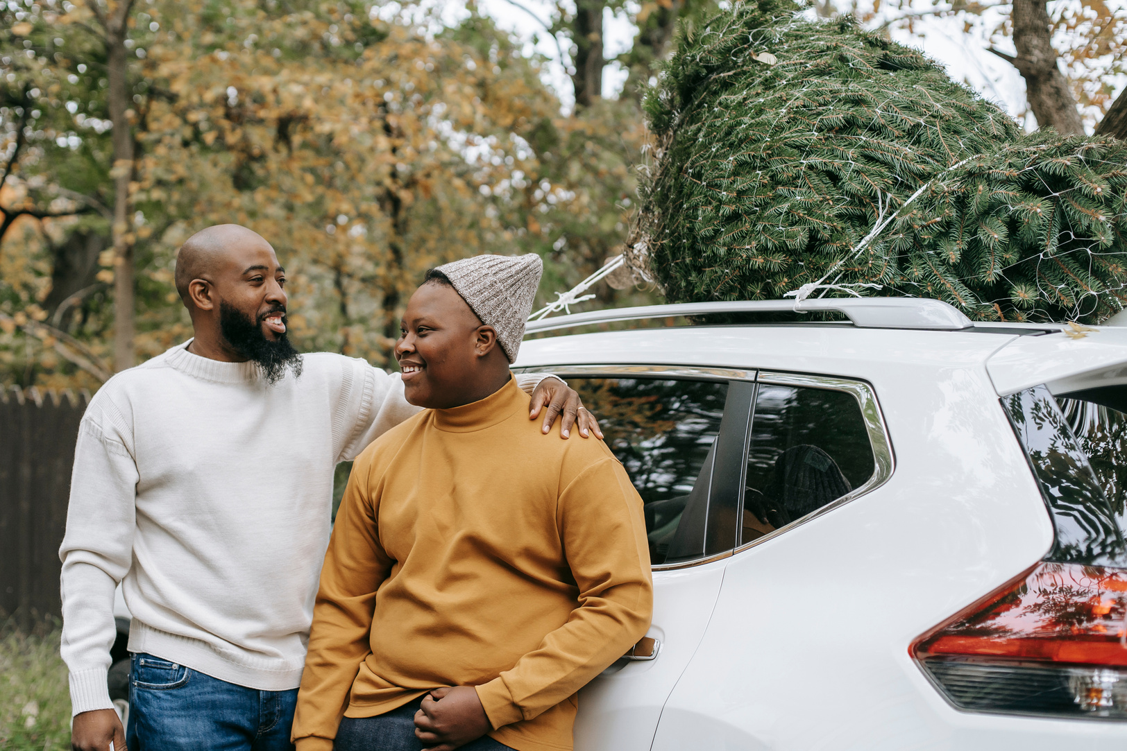 Cheerful bearded black father embracing teen near car in countryside